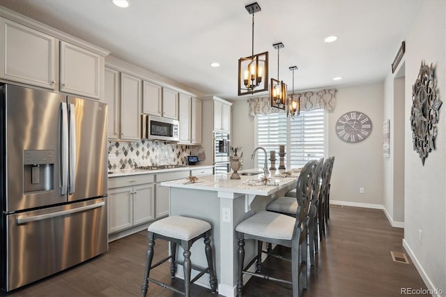 kitchen featuring a kitchen bar, stainless steel appliances, pendant lighting, dark hardwood / wood-style floors, and a kitchen island with sink