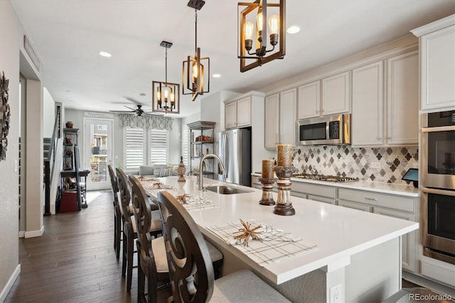 kitchen with dark wood-type flooring, appliances with stainless steel finishes, pendant lighting, and a center island with sink