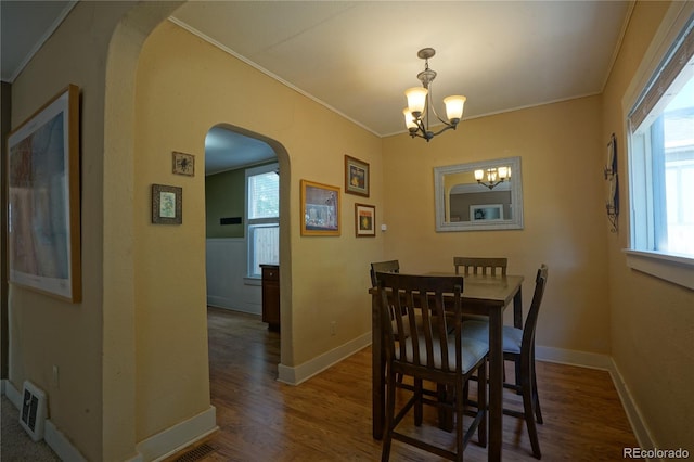 dining area featuring dark wood-type flooring, crown molding, and a notable chandelier