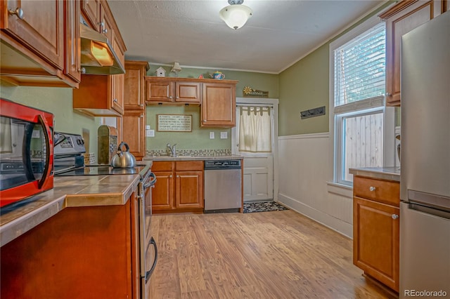 kitchen with tile countertops, stainless steel appliances, sink, crown molding, and light hardwood / wood-style floors