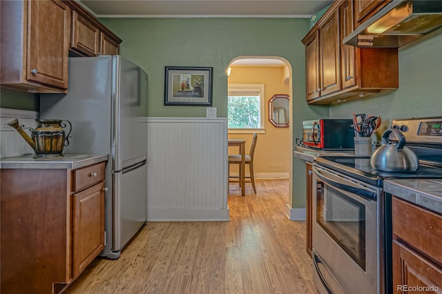 kitchen with ornamental molding, exhaust hood, light hardwood / wood-style flooring, and stainless steel appliances