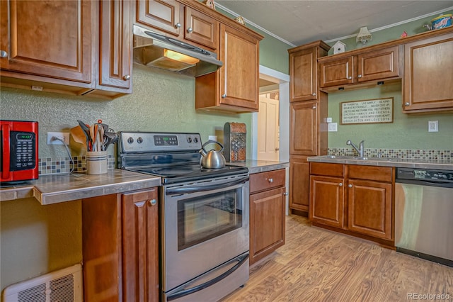 kitchen with appliances with stainless steel finishes, stainless steel counters, light wood-type flooring, crown molding, and sink