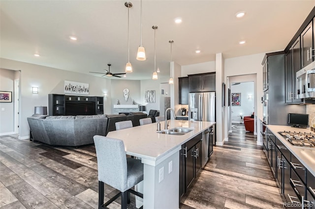 kitchen with a kitchen island with sink, appliances with stainless steel finishes, ceiling fan, a kitchen bar, and sink