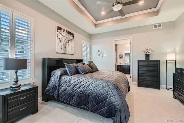 bedroom with a raised ceiling, ceiling fan, light carpet, and connected bathroom