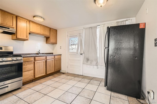 kitchen featuring light tile patterned floors, stainless steel gas range, freestanding refrigerator, and under cabinet range hood