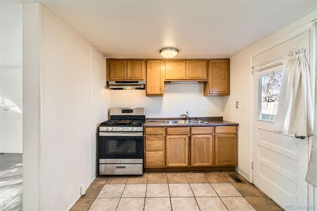 kitchen with light tile patterned floors, dark countertops, gas range, under cabinet range hood, and a sink