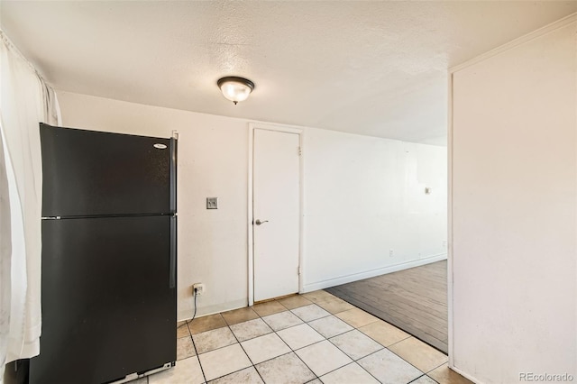 kitchen with light tile patterned floors, freestanding refrigerator, white cabinetry, a textured ceiling, and baseboards