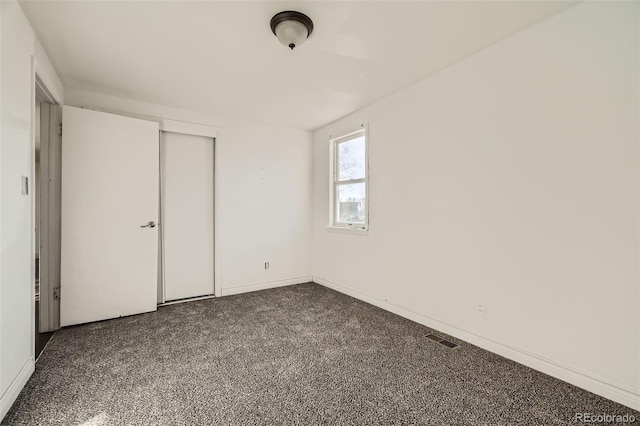 unfurnished bedroom with dark colored carpet, a closet, visible vents, and baseboards