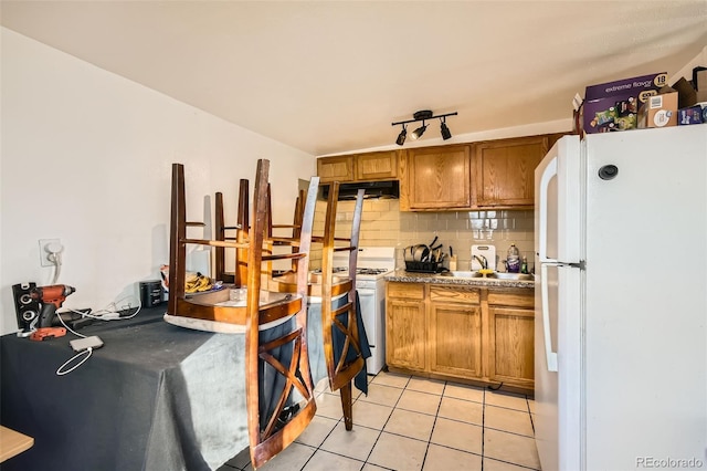 kitchen featuring white appliances, under cabinet range hood, brown cabinets, and backsplash