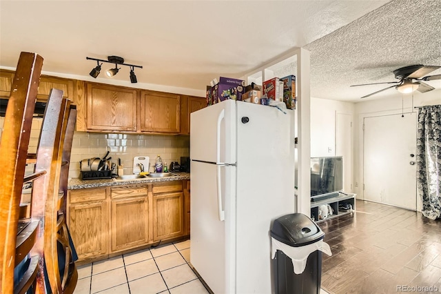 kitchen featuring freestanding refrigerator, brown cabinets, backsplash, and a textured ceiling