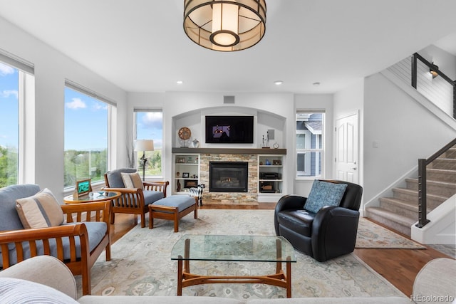 living area with light wood-style floors, stairs, a stone fireplace, and recessed lighting