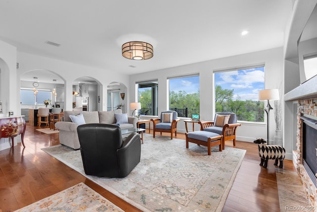 living room with arched walkways, a glass covered fireplace, wood finished floors, plenty of natural light, and recessed lighting