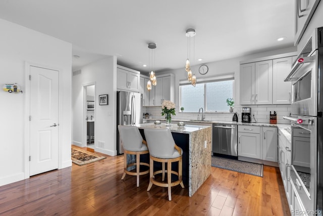 kitchen with stainless steel appliances, a sink, tasteful backsplash, a kitchen island, and light stone countertops