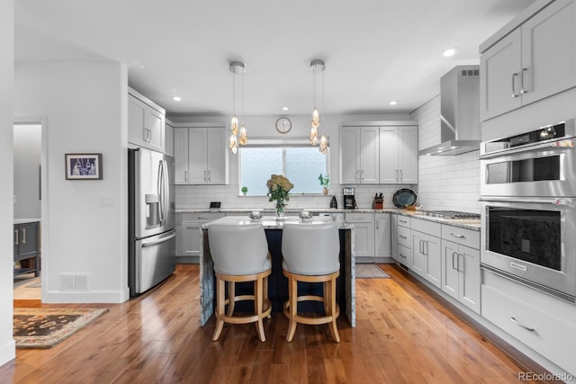 kitchen with appliances with stainless steel finishes, gray cabinetry, wall chimney exhaust hood, light stone countertops, and recessed lighting