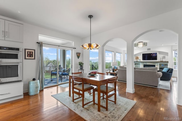 dining area featuring arched walkways, hardwood / wood-style floors, and a fireplace