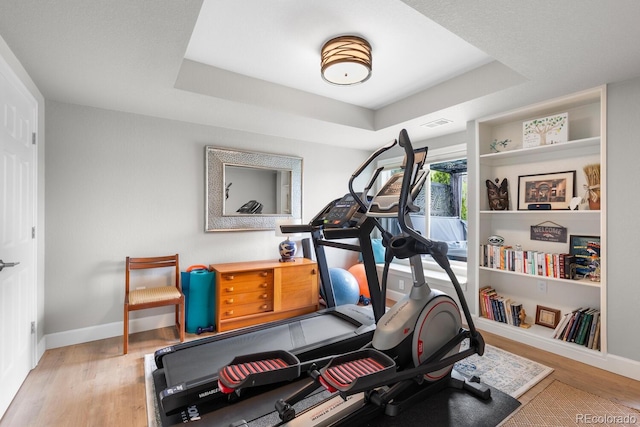 exercise area with a raised ceiling, wood finished floors, and baseboards