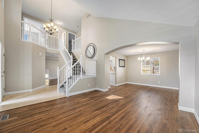 unfurnished living room with baseboards, high vaulted ceiling, an inviting chandelier, and wood finished floors