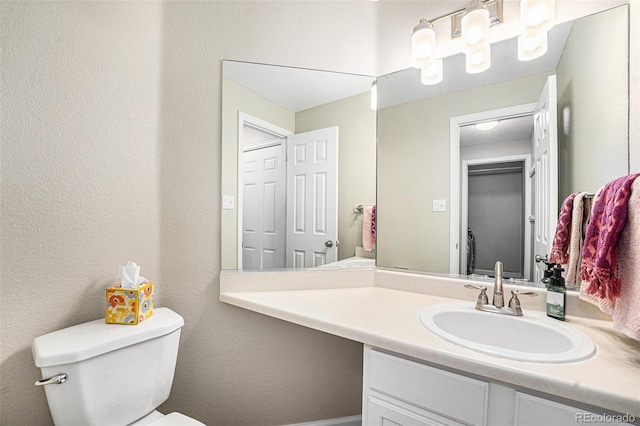 half bathroom featuring toilet, vanity, and a textured wall