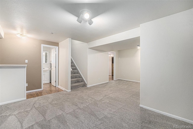 finished basement featuring a textured ceiling, carpet, baseboards, stairs, and a textured wall