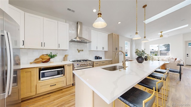 kitchen with a kitchen island with sink, stainless steel appliances, wall chimney range hood, and sink