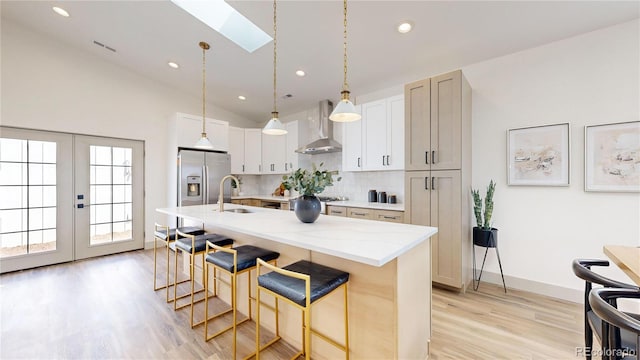 kitchen with a kitchen island with sink, white cabinets, wall chimney exhaust hood, a skylight, and appliances with stainless steel finishes