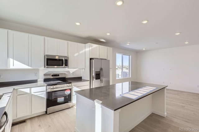 kitchen with a kitchen island, appliances with stainless steel finishes, white cabinets, and light hardwood / wood-style flooring