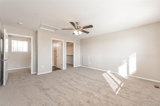 unfurnished bedroom featuring a walk in closet, attic access, carpet flooring, and baseboards