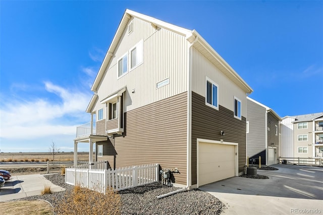 view of side of property with a balcony, concrete driveway, a garage, and fence