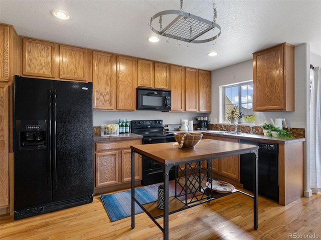 kitchen featuring light hardwood / wood-style floors, black appliances, sink, and a textured ceiling