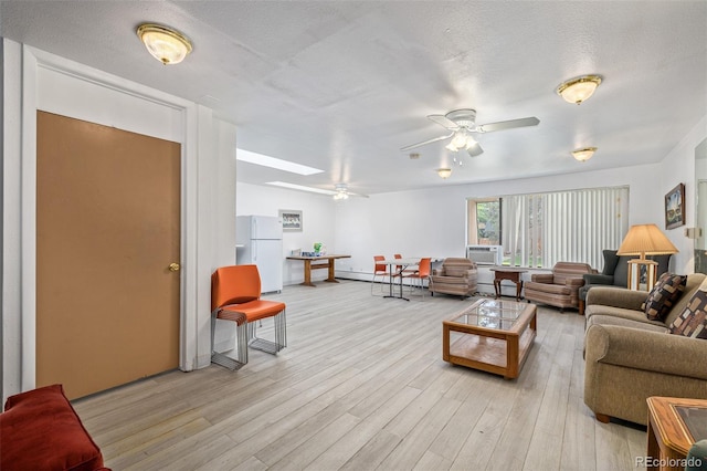 living room featuring ceiling fan, light hardwood / wood-style flooring, a skylight, a textured ceiling, and baseboard heating