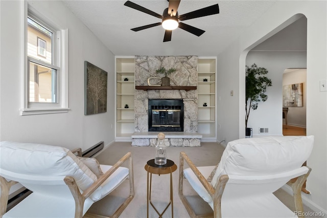 carpeted living room featuring a ceiling fan, visible vents, arched walkways, built in shelves, and baseboards