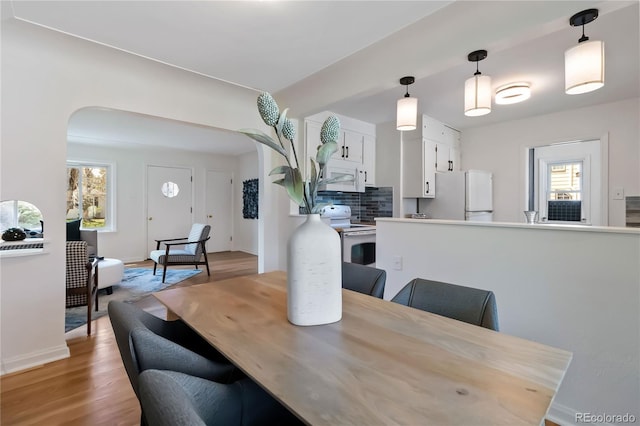 dining room with light wood-style floors, arched walkways, and baseboards