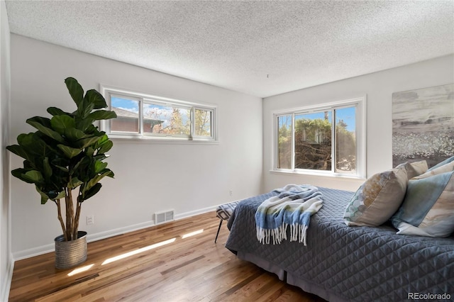 bedroom featuring a textured ceiling, visible vents, multiple windows, and wood finished floors