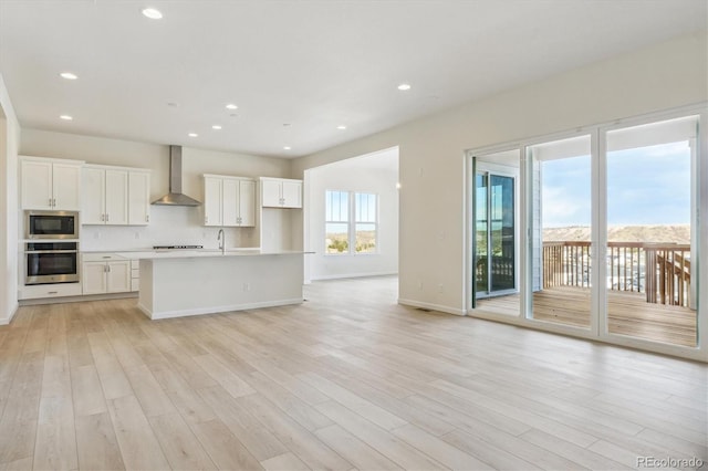 kitchen featuring white cabinets, wall chimney exhaust hood, light hardwood / wood-style floors, and stainless steel appliances