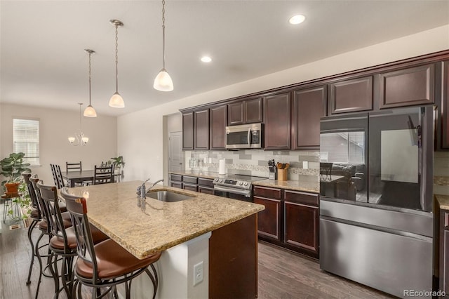 kitchen featuring appliances with stainless steel finishes, a kitchen island with sink, backsplash, dark wood-type flooring, and pendant lighting