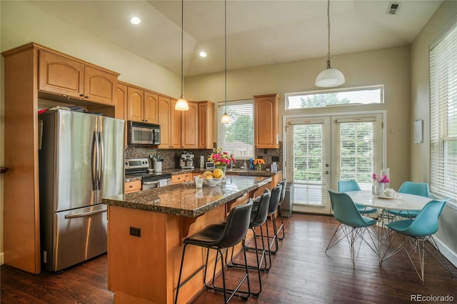 2479 S High St, Denver, CO 80210 - kitchen with appliances with stainless steel finishes, a kitchen island, decorative backsplash, dark wood-style flooring, and a kitchen bar