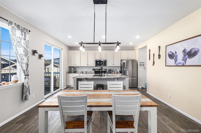 kitchen featuring pendant lighting, appliances with stainless steel finishes, a kitchen island with sink, white cabinetry, and light stone counters