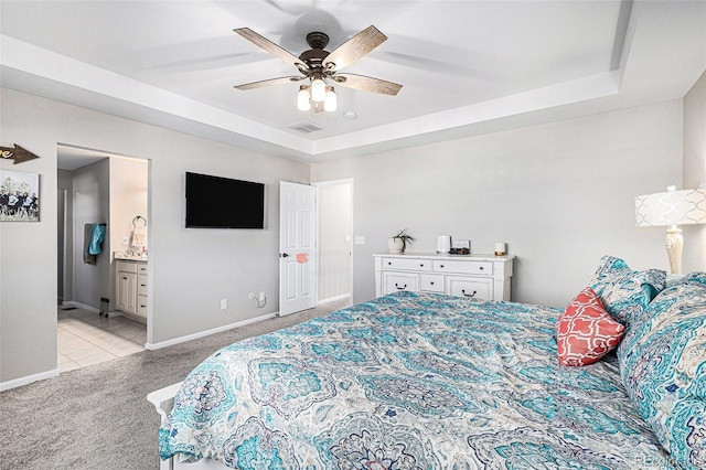 bedroom with connected bathroom, light colored carpet, ceiling fan, and a tray ceiling