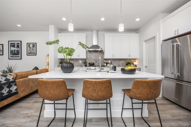 21482 E 60th Ave, Aurora, CO 80019 - kitchen with high quality fridge, wall chimney range hood, a breakfast bar area, light wood-style floors, and decorative backsplash