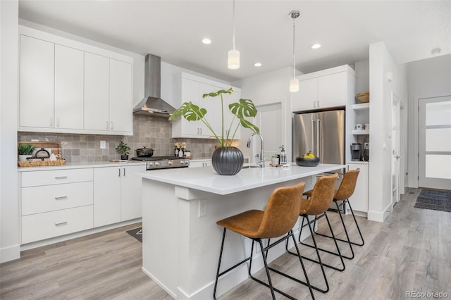 21482 E 60th Ave, Aurora, CO 80019 - kitchen featuring wall chimney exhaust hood, high quality fridge, tasteful backsplash, a kitchen bar, and light wood-style floors