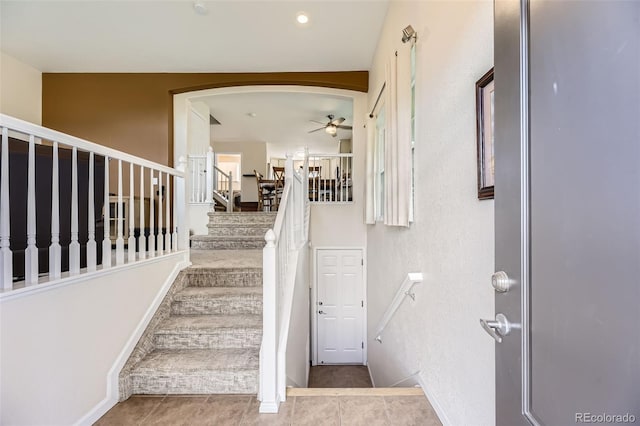 staircase featuring arched walkways, ceiling fan, baseboards, and tile patterned flooring