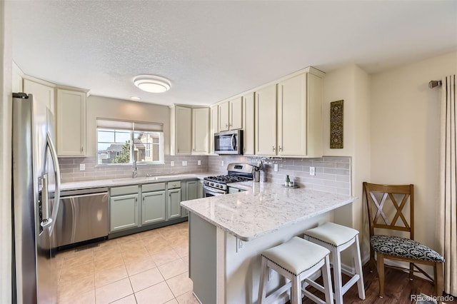 kitchen with a peninsula, a sink, appliances with stainless steel finishes, and tasteful backsplash