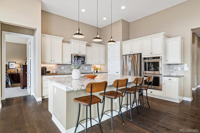 kitchen with hanging light fixtures, white cabinetry, appliances with stainless steel finishes, and a kitchen island with sink