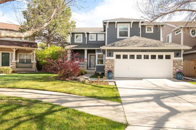 view of front of house with a shingled roof, stone siding, a front yard, concrete driveway, and covered porch