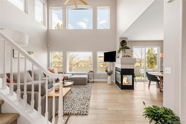 living area featuring stairs, light wood-type flooring, a multi sided fireplace, and a towering ceiling