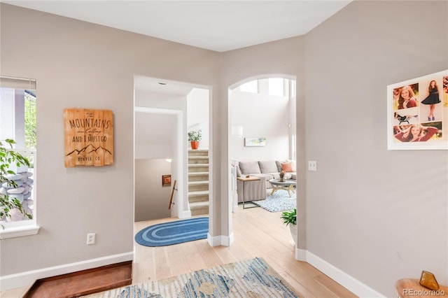 corridor featuring light wood-style floors, arched walkways, baseboards, and stairway
