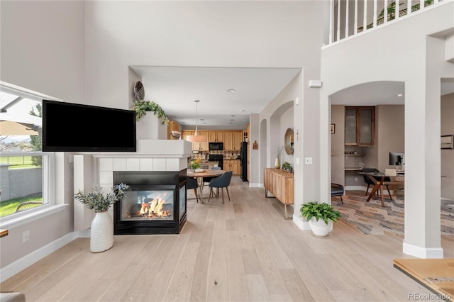living room featuring a high ceiling, a fireplace, arched walkways, light wood-style flooring, and baseboards