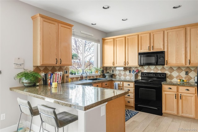 kitchen featuring tile counters, a kitchen breakfast bar, light brown cabinetry, and black appliances