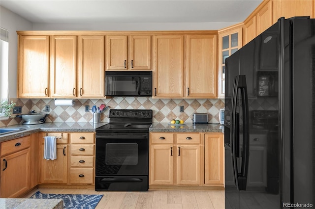 kitchen featuring backsplash, light brown cabinetry, glass insert cabinets, and black appliances
