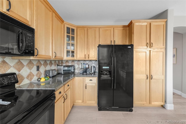 kitchen featuring tasteful backsplash, a toaster, black appliances, dark stone countertops, and glass insert cabinets